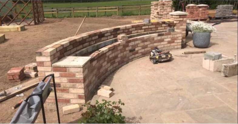 Curved reclaimed brick garden wall being built beside a sandstone patio