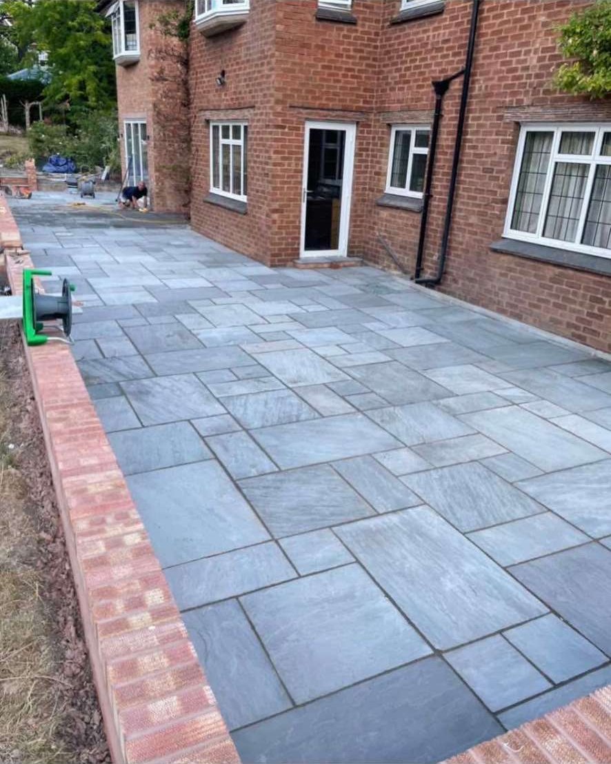 Grey Indian sandstone patio with brick edging around a red brick house