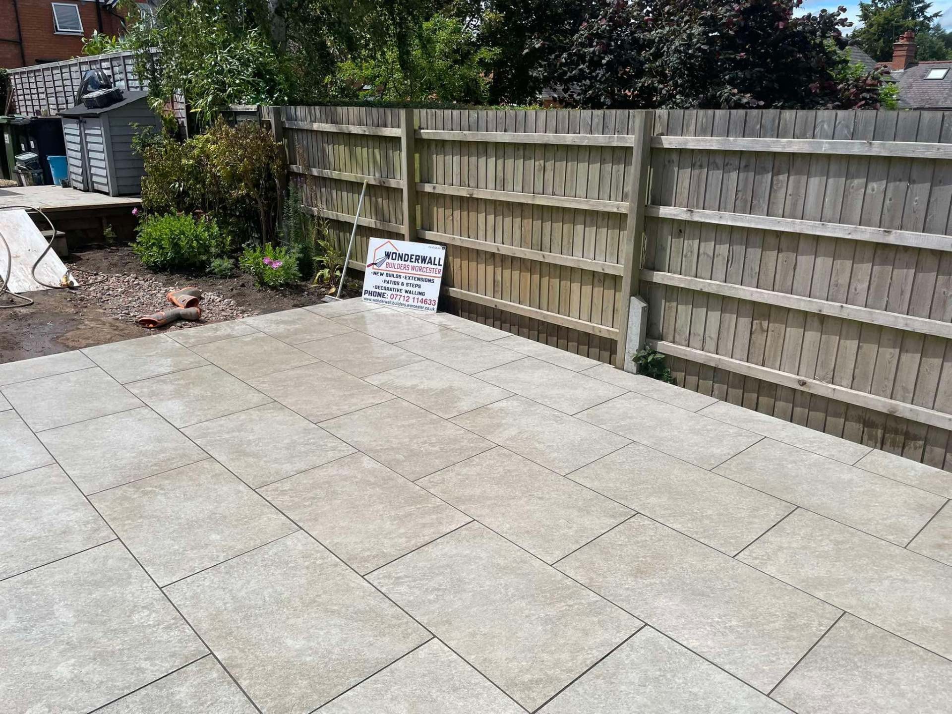 Large light porcelain patio laid in a rear garden with Wonderwall site board