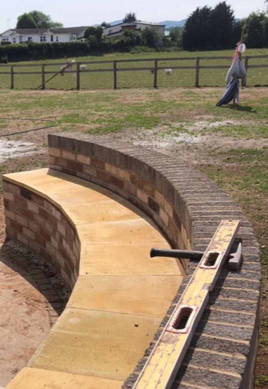 Curved brick garden wall with stone bench seating and paved base