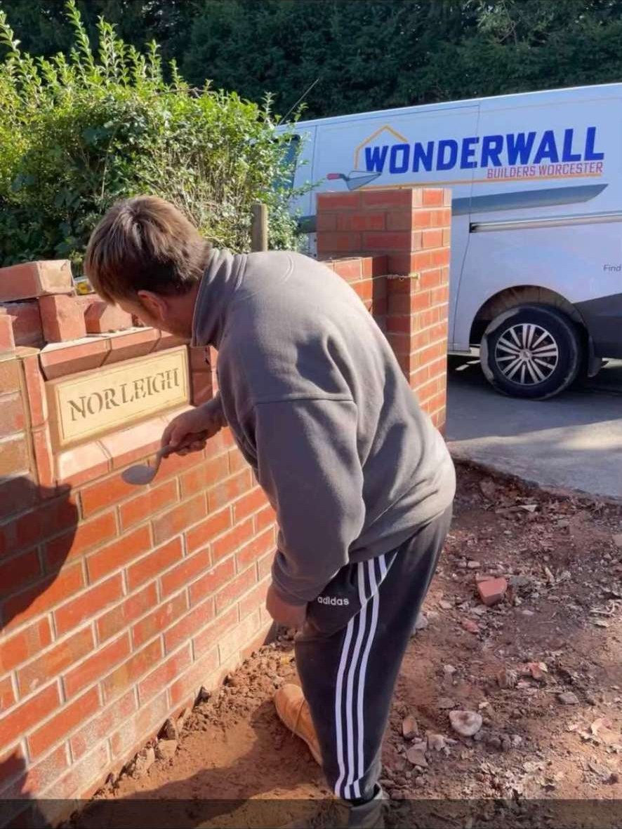 Bricklayer pointing a red brick wall with a carved stone nameplate